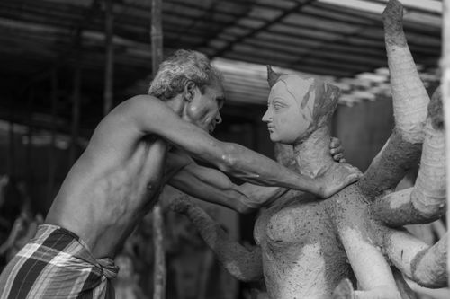Free A shirtless elderly man intensely sculpts a detailed statue in a workshop. Stock Photo