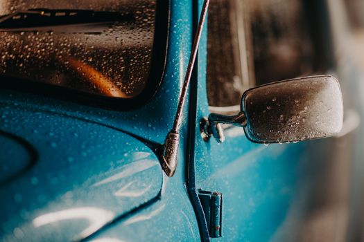 A detailed view of a wet blue vintage car showcasing water droplets on the surface and side mirror.