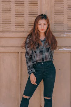 一位时尚的年轻女子身着牛仔牛仔裤和格子衬衫，在木制背景前自信地摆着姿势