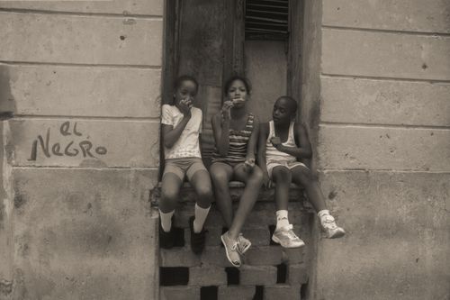 Free Three kids sitting on steps, eating popsicles in an urban setting. Monochrome photo. Stock Photo