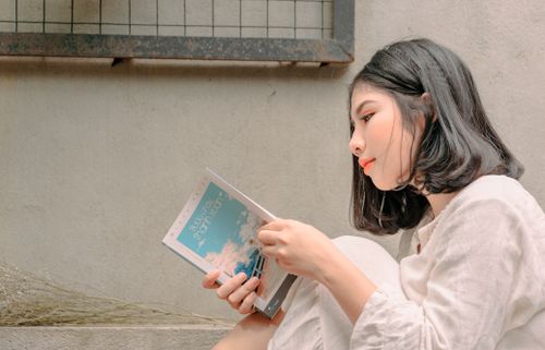 Free A young woman deeply engaged in reading a book while sitting outdoors, captured in natural daylight. Stock Photo