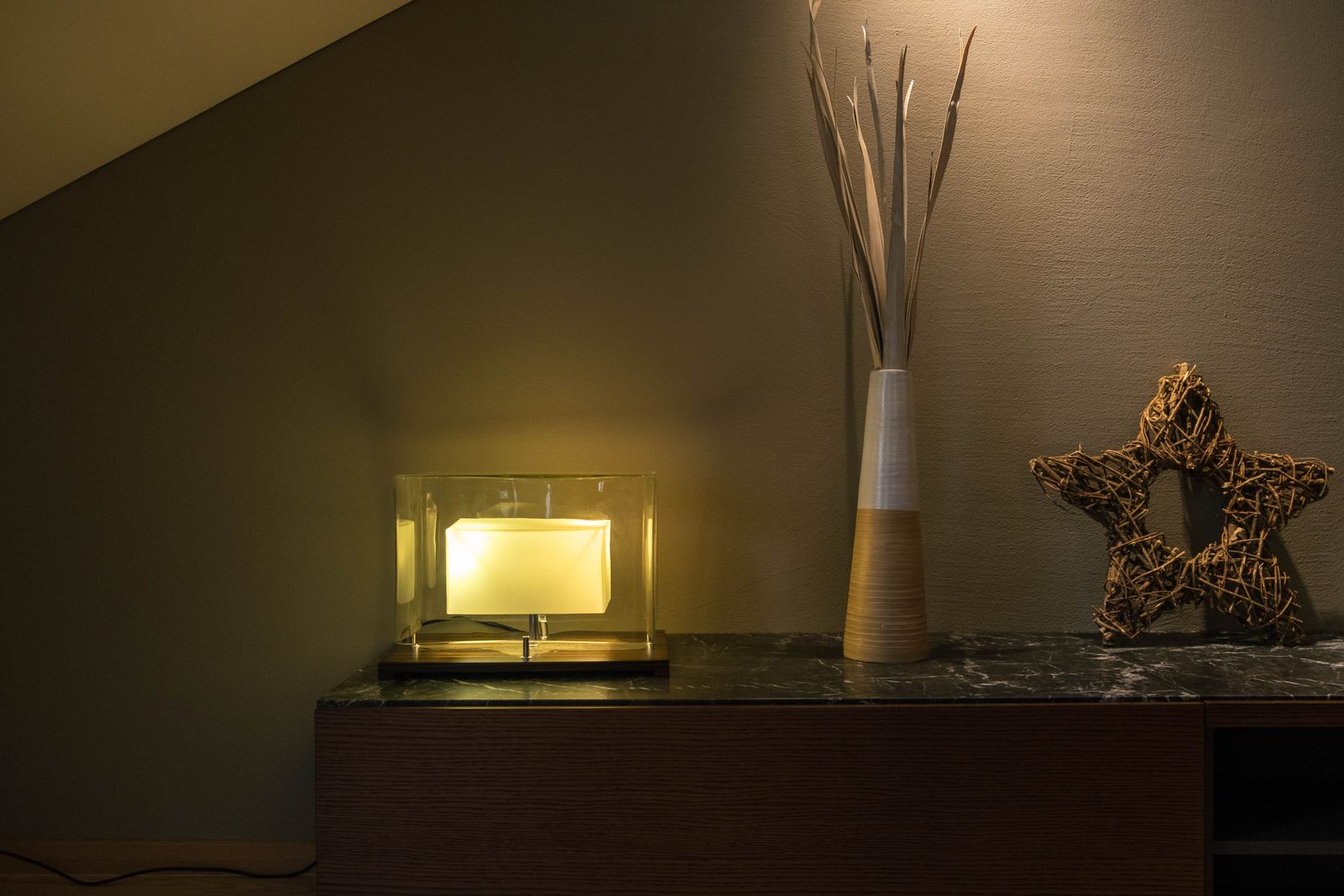 A modern lamp beside a tall vase with twigs and a decorative star on a shelf.