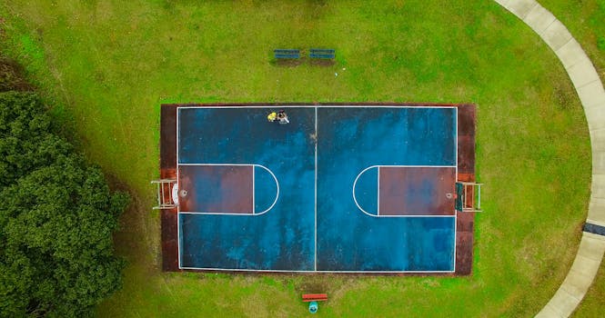 Top-down view of a vibrant outdoor basketball court set in a lush green park, captured brilliantly from above.