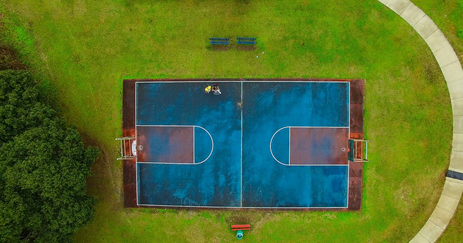 Quadra de basquete ao ar livre vista de cima, cercada por vegetação verde