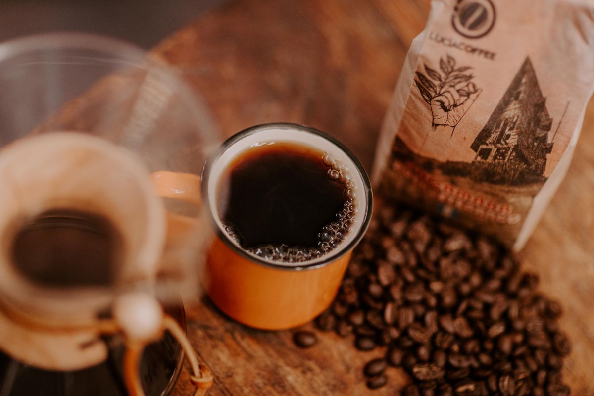 Cup of coffee next to roasted beans and a coffee bag