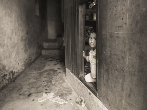 Free A young child peeks out from a rustic doorway. Sepia tones enhance the vintage feel. Stock Photo