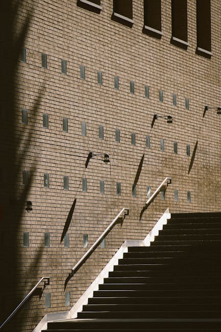 A modern staircase with a brick wall and unique shadow pattern, captured outdoors in daylight.