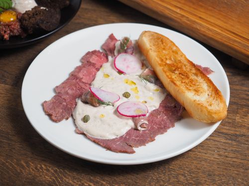 Free Sliced beef with creamy sauce and radishes on a white plate, served with toasted bread. Stock Photo