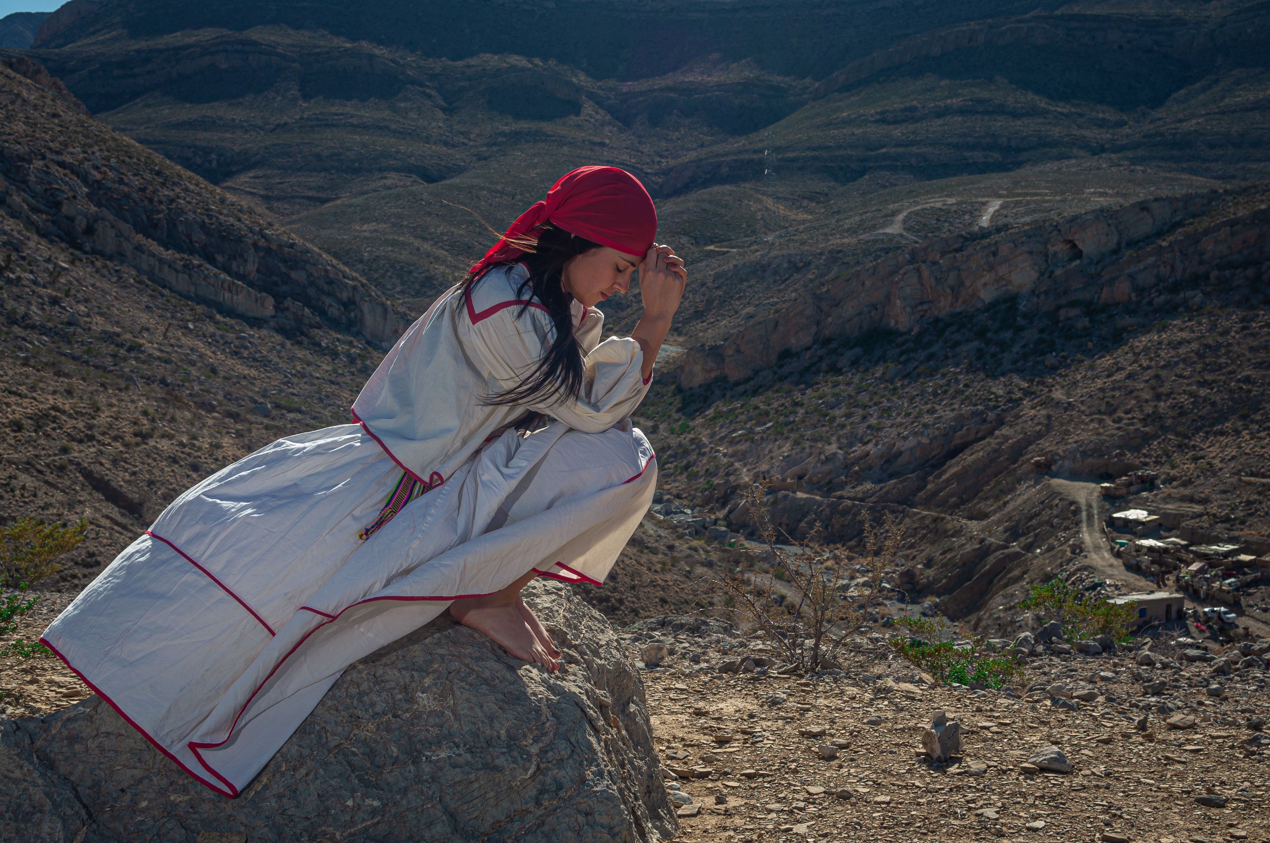 Woman wearing traditional clothing and praying in a mountainous region, representing cultural heritage.