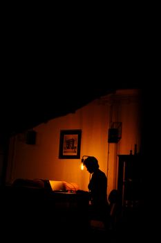 A silhouette of a woman working at a desk under a warm lamp in a dark room.