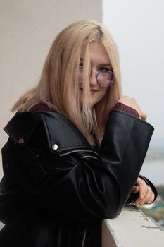 Portrait of a young woman with blonde hair in a leather jacket wearing sunglasses, smiling.