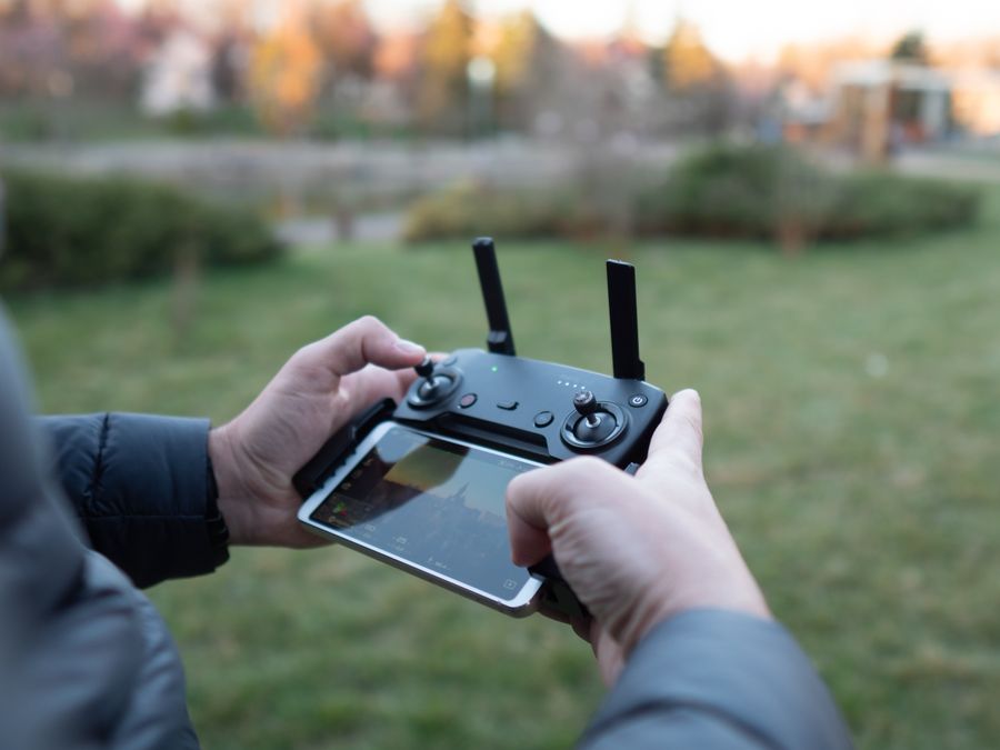 A pilot's hands on a drone controller with the live camera feed on the screen