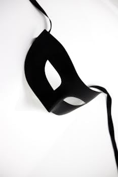 A sophisticated black masquerade mask lying on a white surface, symbolizing mystery and elegance.