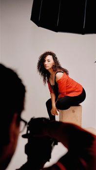 A woman posing in a studio setup while a photographer captures her portrait with professional lighting.