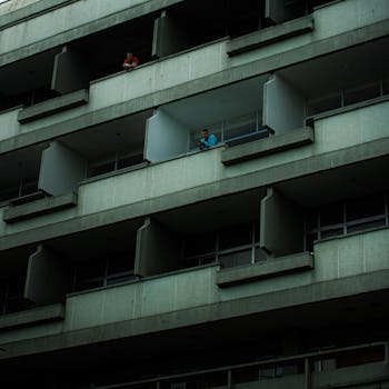 Concrete residential building with balconies, featuring people looking out.