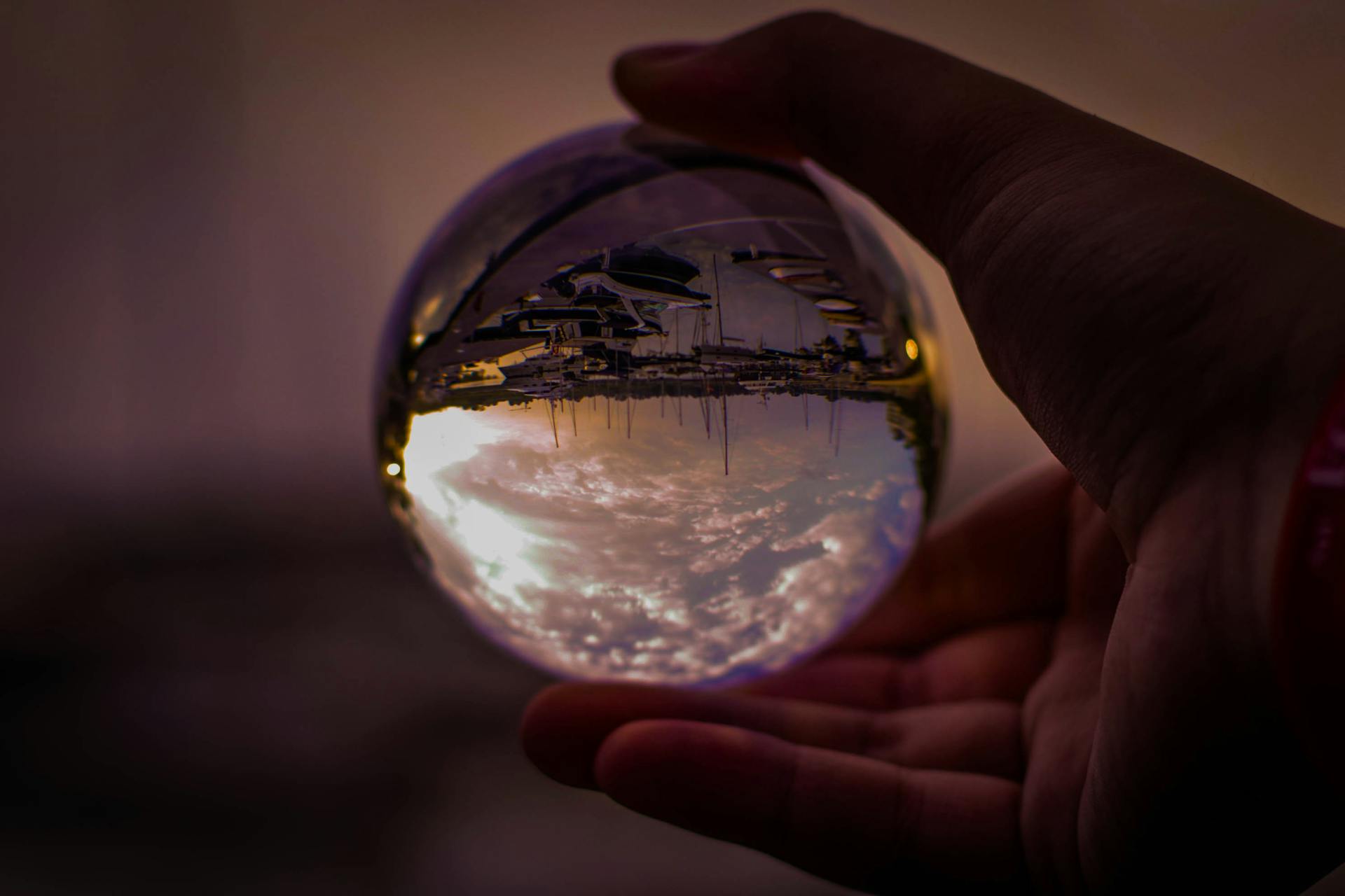 A mesmerizing view through a crystal ball reflecting a sunset at the harbor, held in a hand.