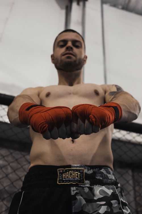 Free Shirtless boxer with wrapped fists stands confidently in gym, ready for a match. Stock Photo