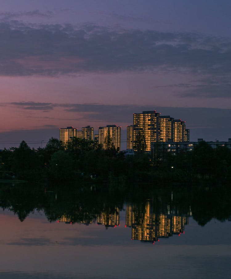 Reflection In Water Near City At Dusk