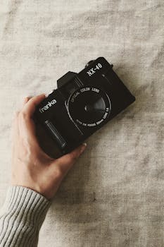 A vintage Franka NX-40 camera held by a hand, placed on a linen fabric surface.