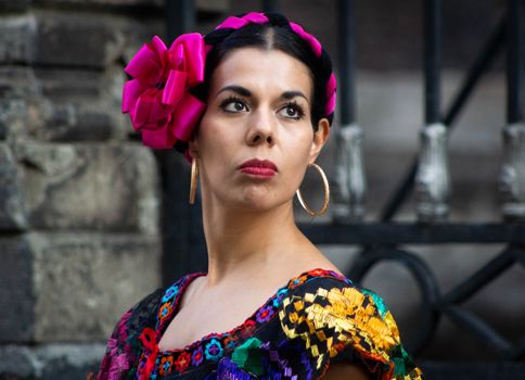 Portrait of a woman in traditional Mexican attire with colorful floral details and earrings.