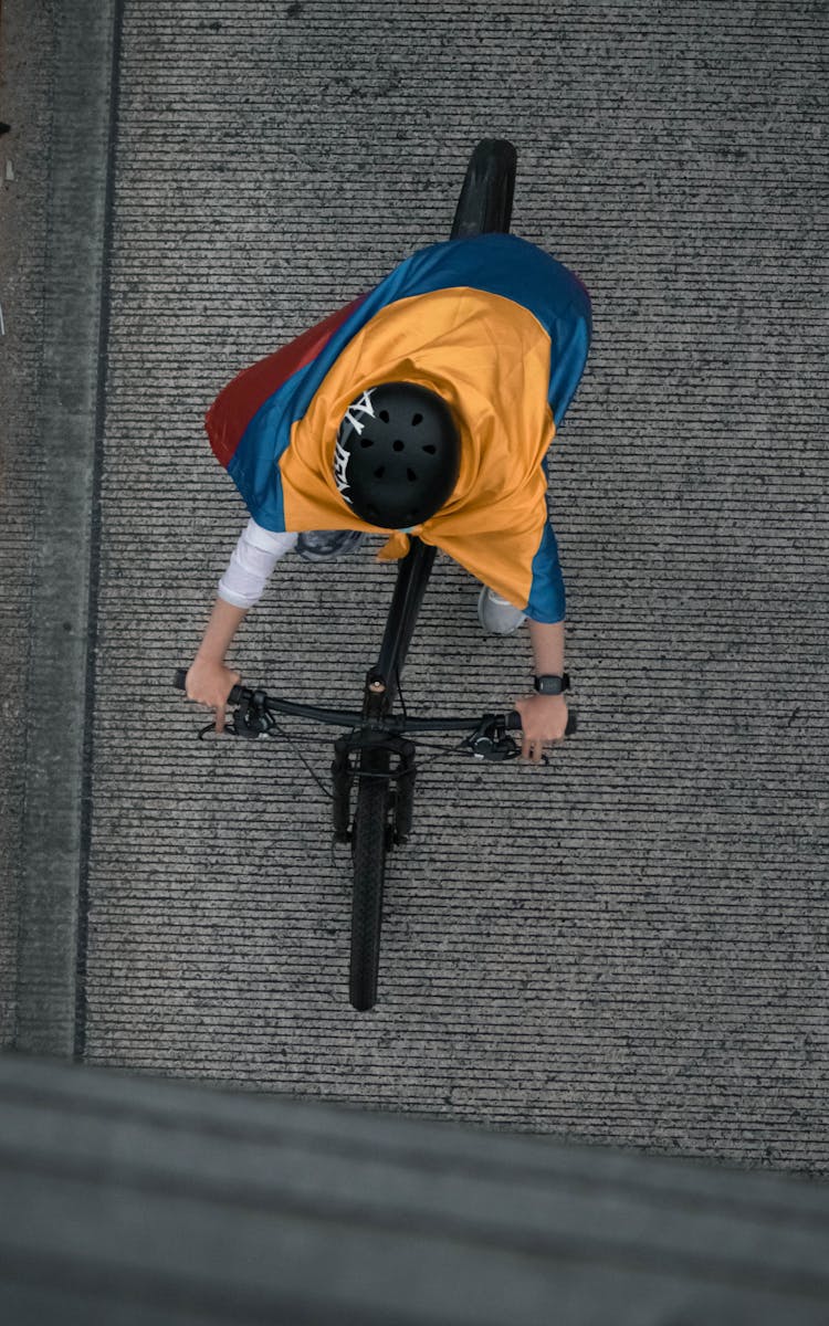 Child Riding On Black Bicycle Wearing Helmet And Cape