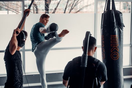 Three men engaged in a dynamic kickboxing workout session in a modern gym environment.