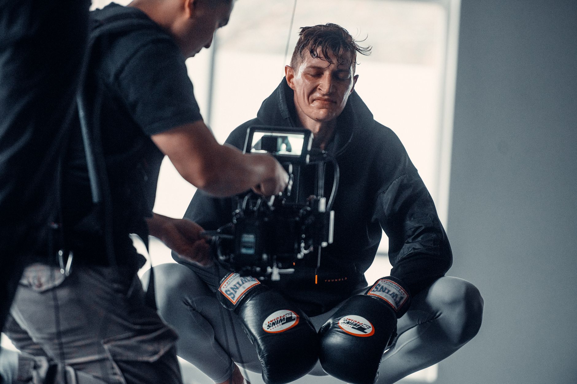A boxer crouches in studio, with a camera crew capturing the moment, showcasing determination and athleticism.