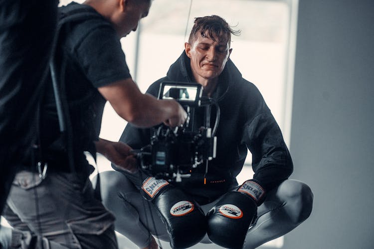 Man In Black Hoodie Jacket And Black Boxing Gloves In Crouching Position Beside A Cameraman