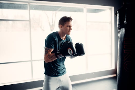 A young male boxer practicing punches with a heavy bag indoors.