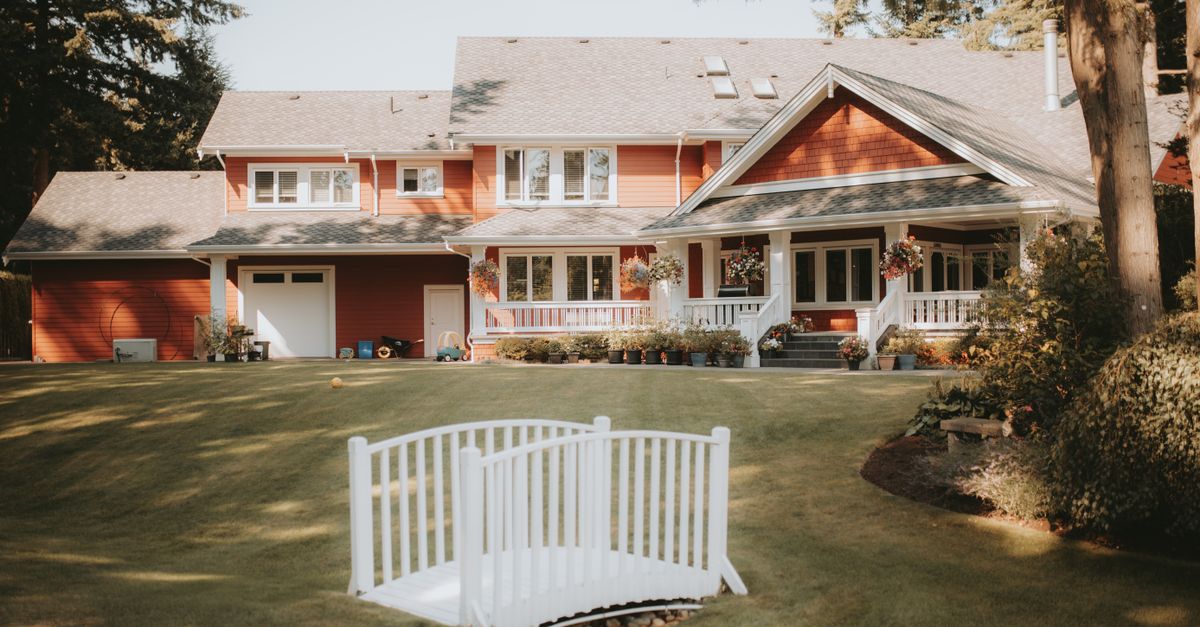 Charming red house with a large yard and white bridge, perfect for a peaceful lifestyle.