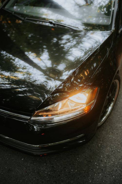 Free Close-up of a sleek black car with highlighted headlight on a road surrounded by nature. Stock Photo