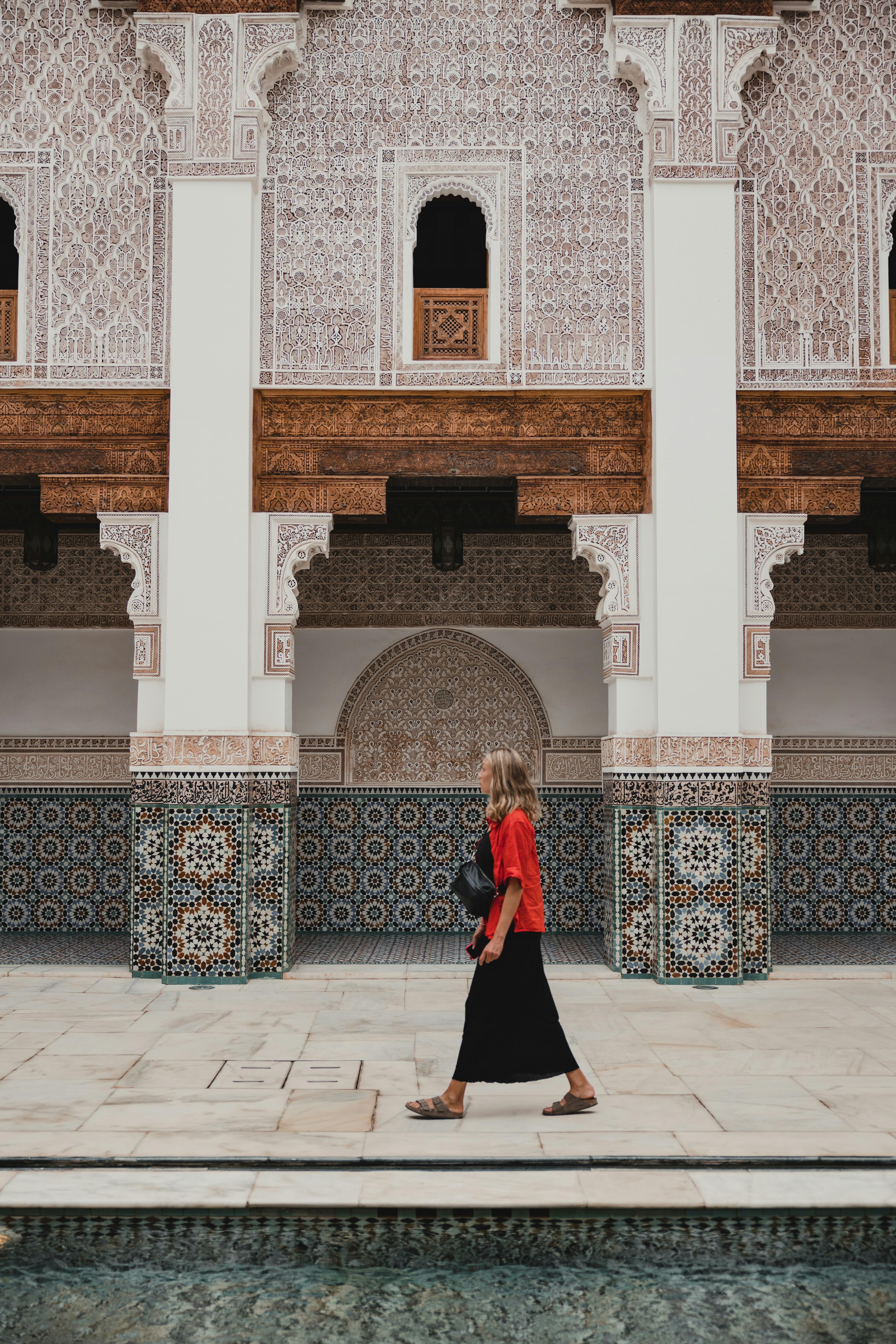 A woman in red walks through a beautifully decorated Islamic architectural courtyard, displaying intricate patterns.