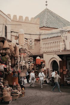 Lively street market in Morocco with people shopping and traditional crafts displayed.