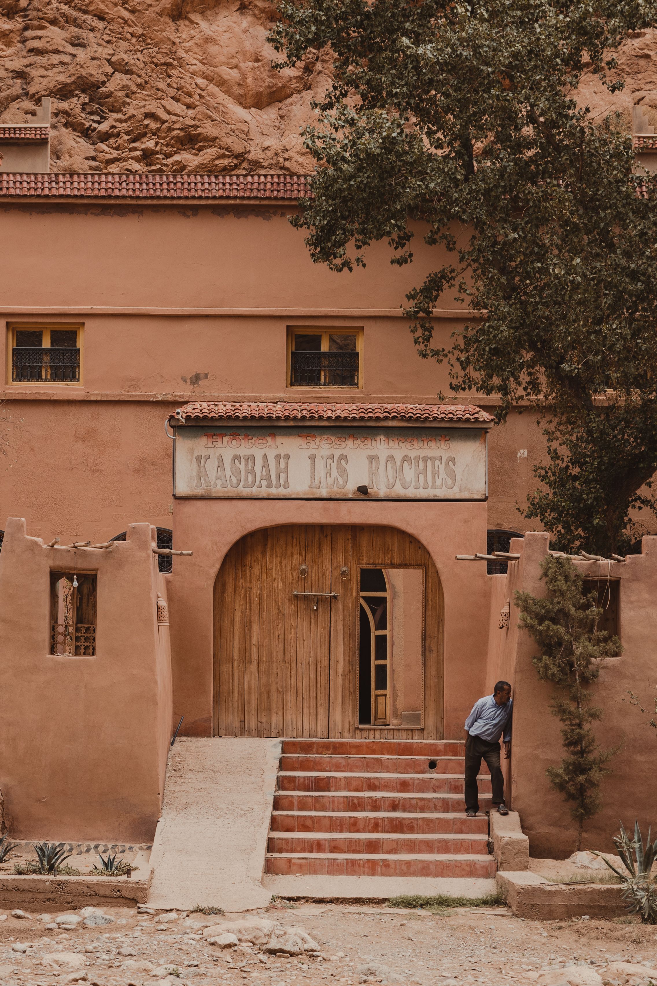 A man stands by the entrance of Kasbah Les Roches, set against a rocky backdrop.
