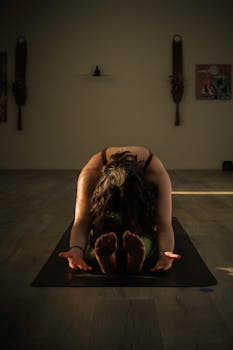 A woman performs a yoga stretch in a dimly lit studio, creating a peaceful atmosphere.