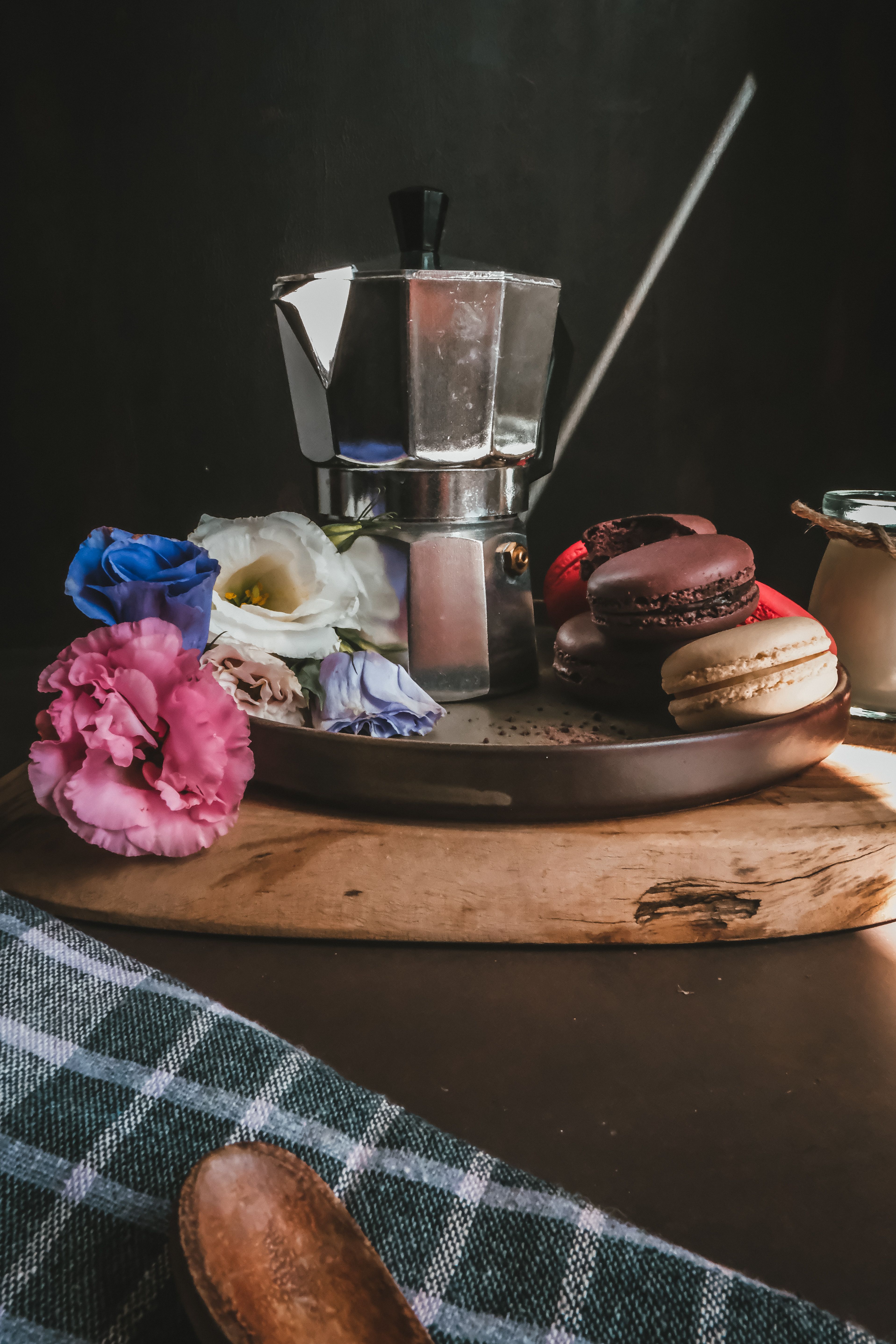 A stylish arrangement of a coffee maker with macarons and flowers on a wooden board.