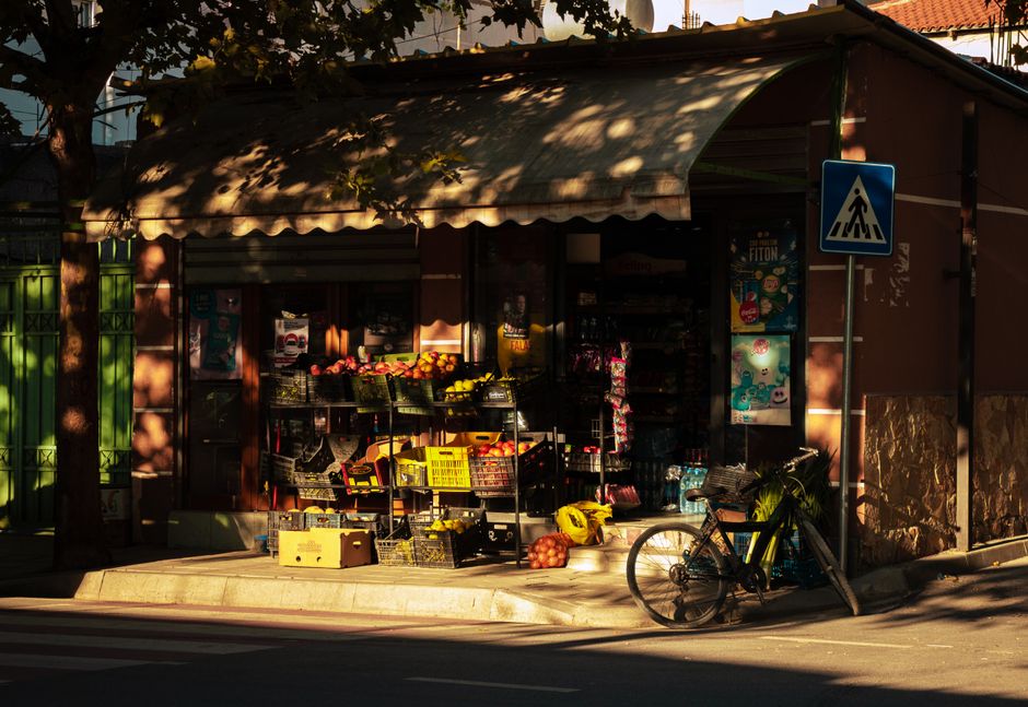 A vibrant fruit stall displaying fresh produce on a sunlit street corner in Tirana, Albania.