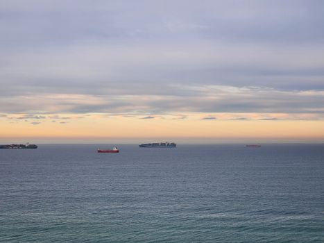 Serene ocean view with cargo ships under a colorful twilight sky.