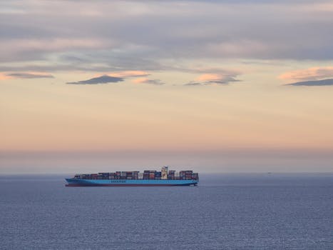 A cargo ship sails on calm waters during a pastel-hued twilight.