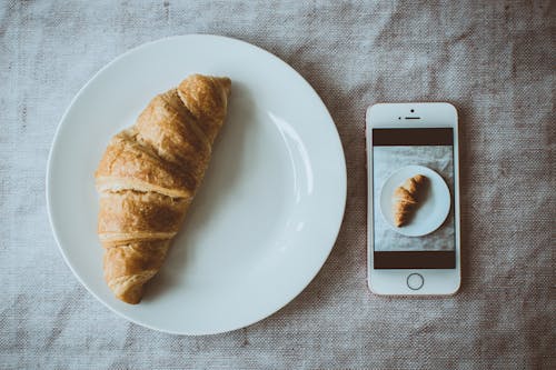 Pane Croissant Sulla Piastra Bianca Rotonda Accanto A Iphone Se In Oro Rosa Visualizzazione Di Foto Di Pane Croissant Sulla Piastra