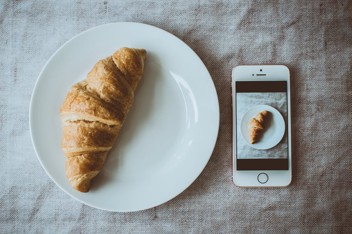 免费 玫瑰金iphone Se旁边的圆形白板上的牛角面包，在板上显示牛角面包的照片 素材图片