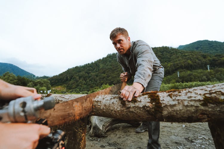 Person Filming A Man Sawing Through A Tree Log 