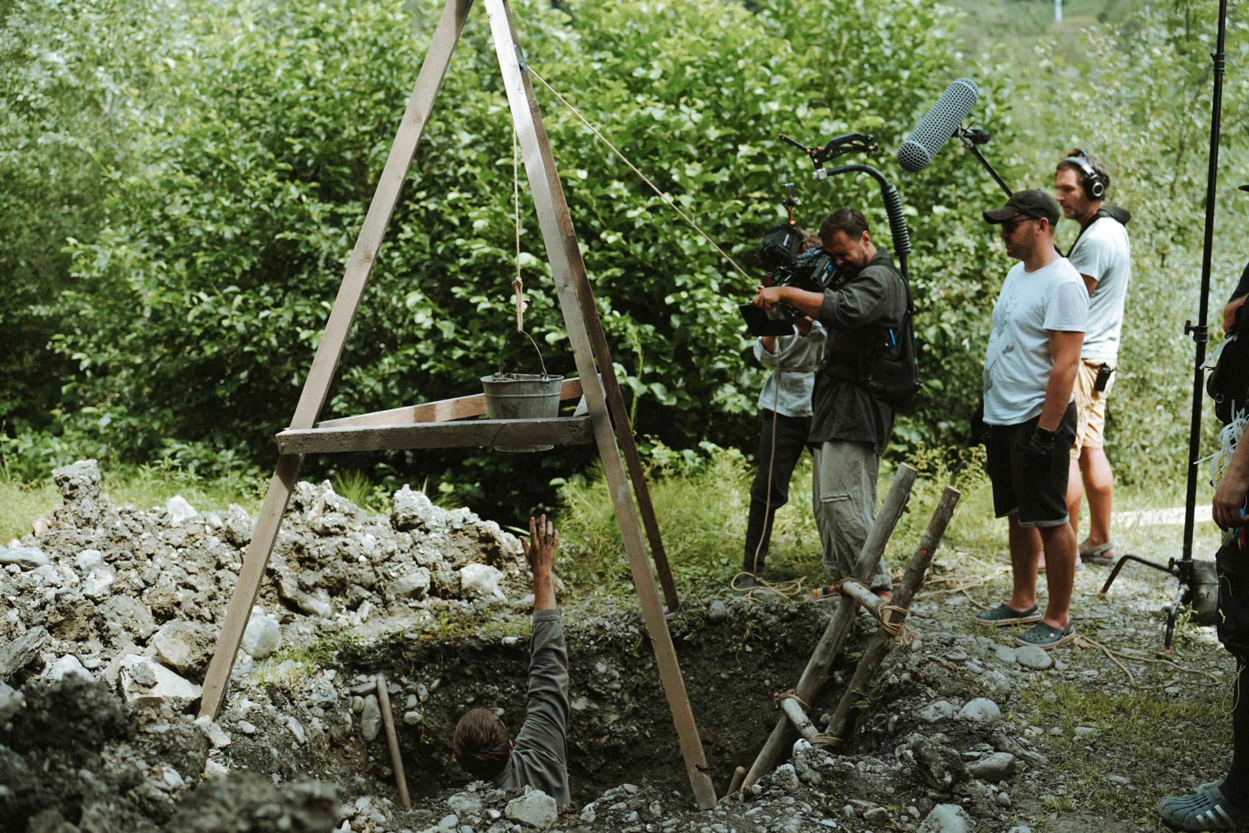 people filming man reaching bucket from hole