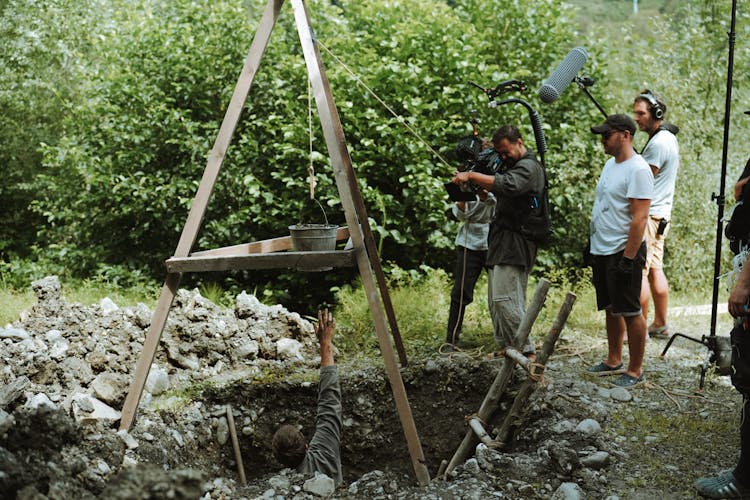 People Filming Man Reaching Bucket From Hole