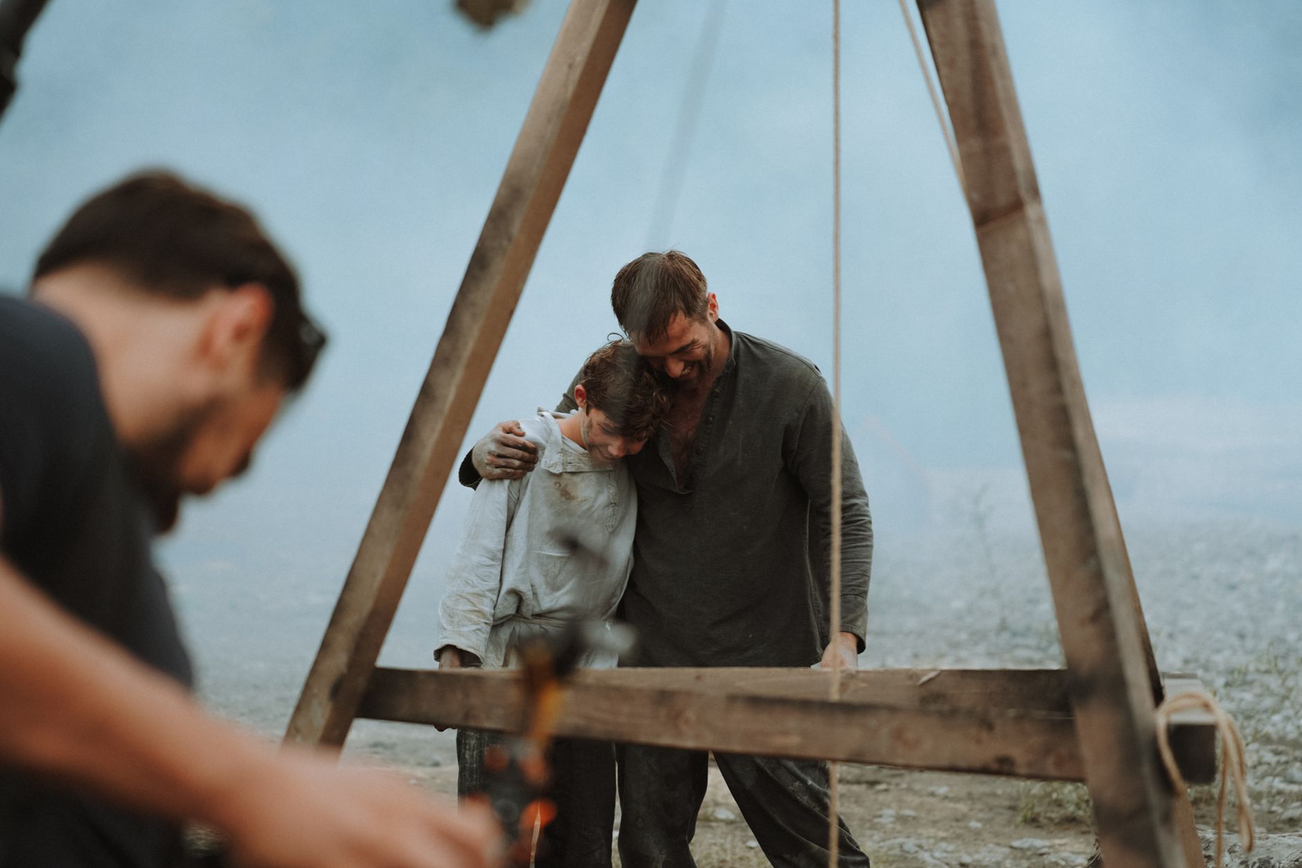 A heartwarming moment of a father and son embracing outdoors amidst smoke. Captured in a natural setting.