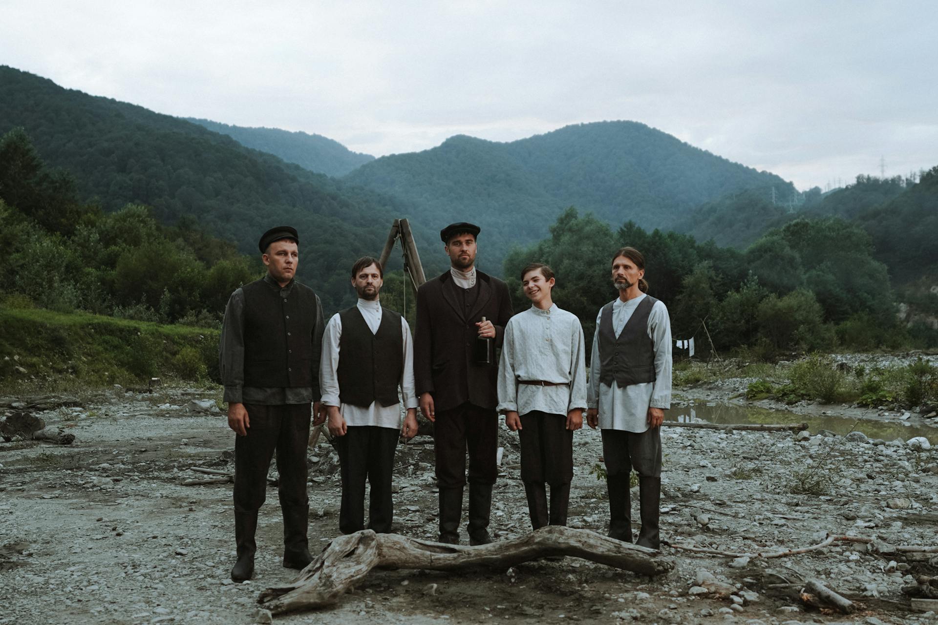 Five miners in traditional attire posing in a serene mountainous landscape during daytime.