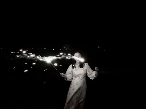 A Grayscale Photo of a Woman in White Dress Holding Sparklers