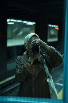 Focused woman capturing a moment in a subway station through a camera lens.