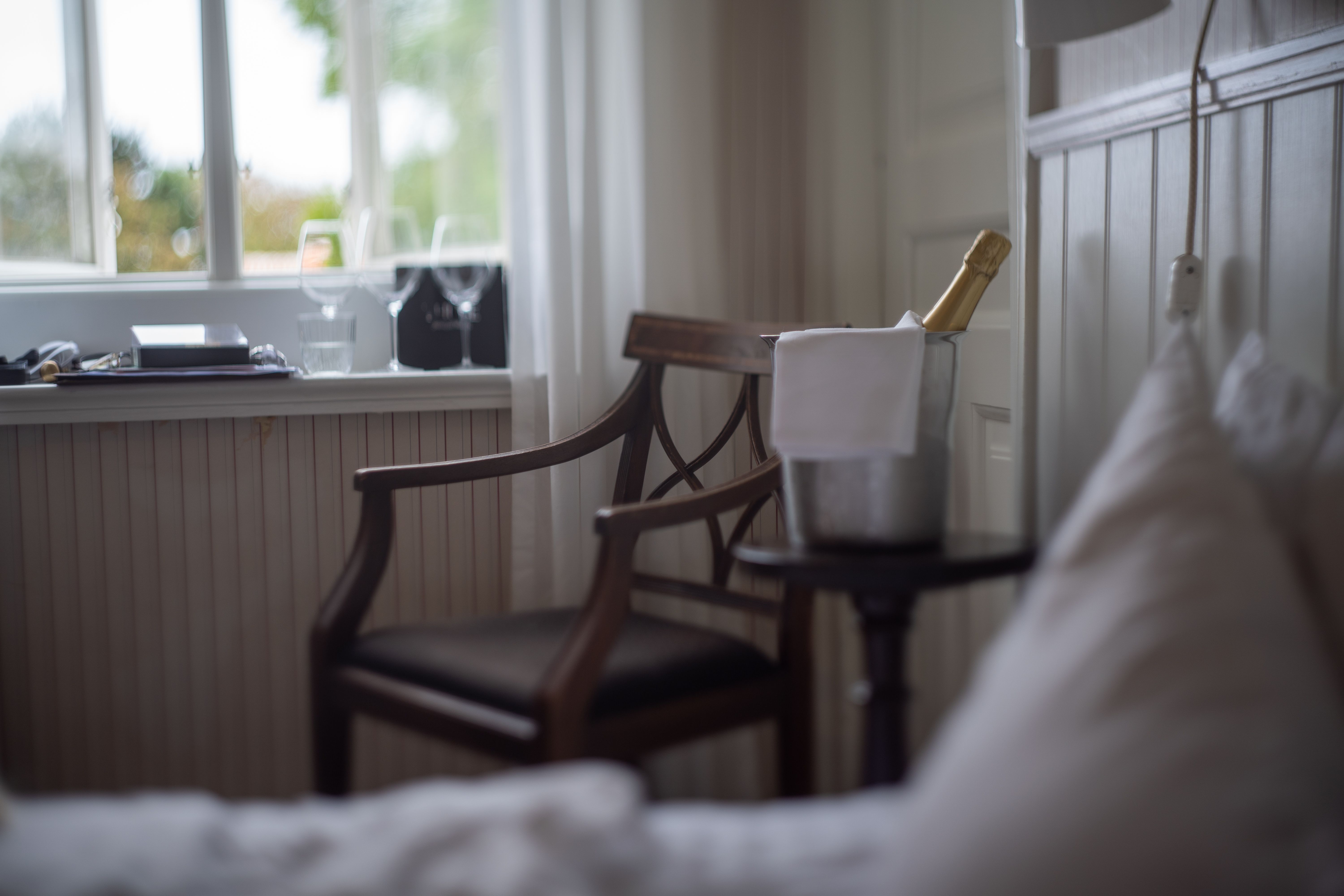 A serene indoor scene featuring a champagne bucket on a table beside a wooden chair.