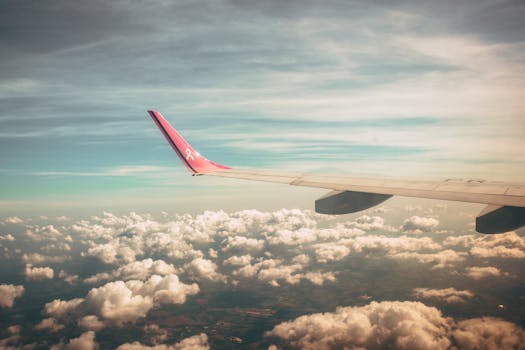 A picturesque view from an airplane window, capturing the wing against a backdrop of fluffy clouds and a vibrant sky at dawn.